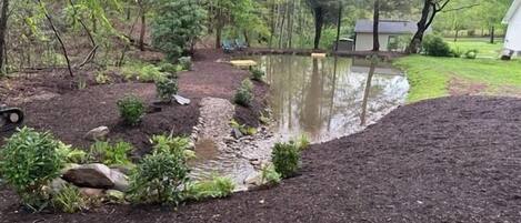 Ein Garten mit Teich, umgeben von Bäumen und einer kleinen Gartenhütte.