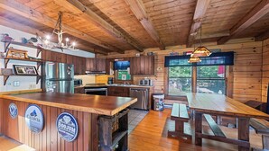 A rustic cabin interior with wooden walls, a wooden ceiling, a kitchen with modern appliances, a bar area, and a dining table. - 2BD 2BA Cozy Log Cabin, Easy Paved Access, View, Gas Log, Hot Tub, Wifi Pond (Waynesville)