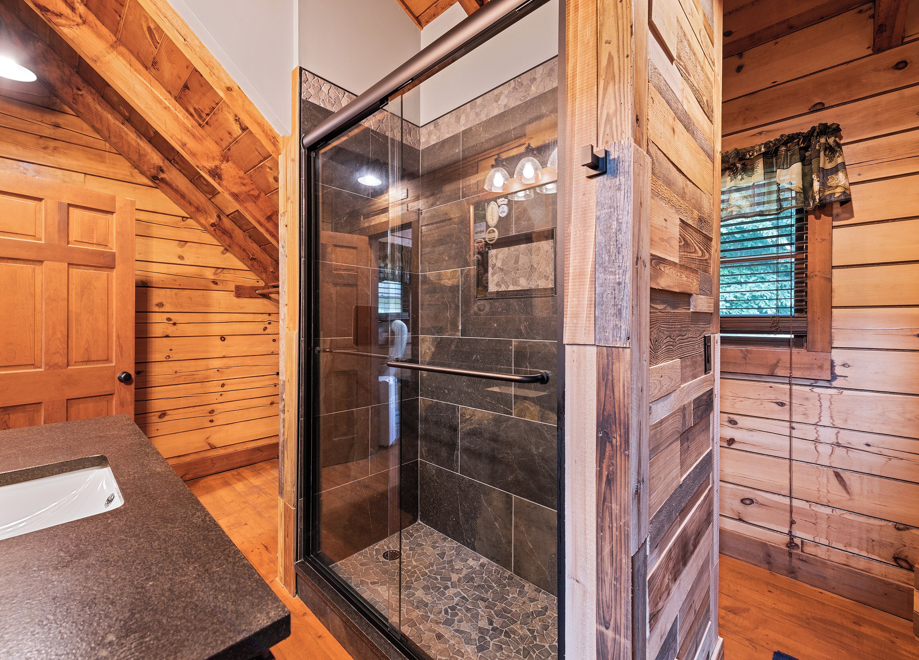 A shower with glass doors, wooden walls, and a tiled floor.