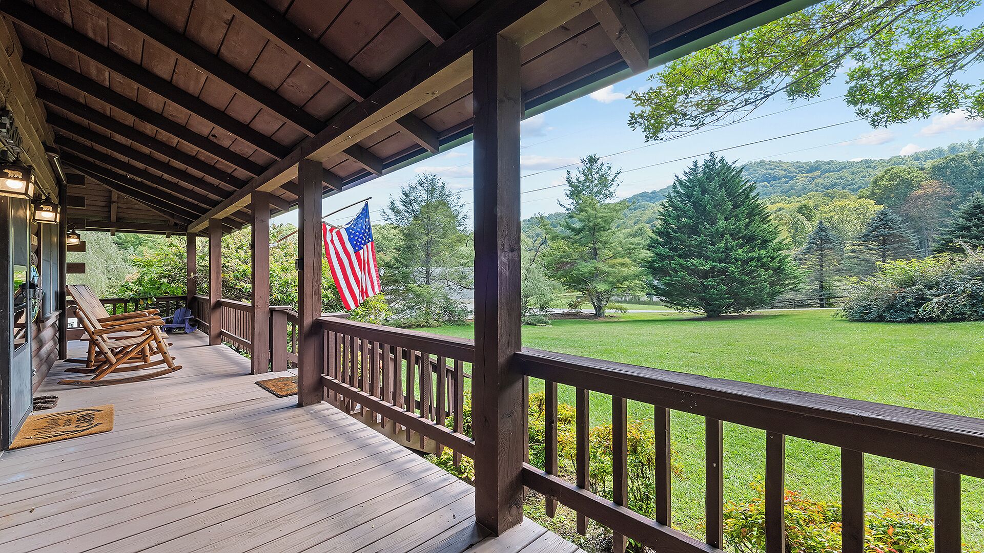 A wooden porch with a view of a grassy landscape and trees.