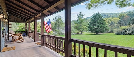 A wooden porch with a view of a grassy landscape and trees.