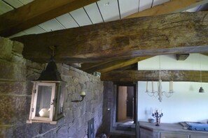 Un interior rústico con vigas de madera a la vista, pared de piedra, un farol y una araña.