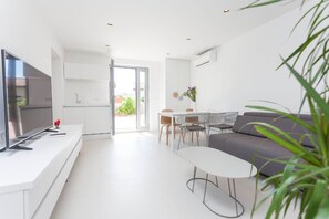 Ein modernes Wohnzimmer mit Fernseher, Essbereich mit Tisch und Stühlen sowie ein graues Sofa.