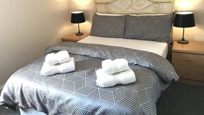 A neatly made bed with a geometric patterned bedspread, two bedside tables with lamps, and a wall with three framed pictures. - Princetown Guesthouse (Bangor)
