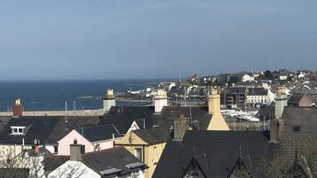 Un pueblo costero con edificios residenciales, un faro destacado y un puerto deportivo lleno de barcos.
