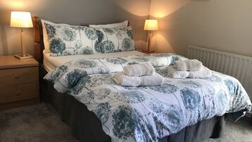 Una cama bien tendida con ropa de cama floral, dos lámparas de noche, una mesita de noche y un radiador.