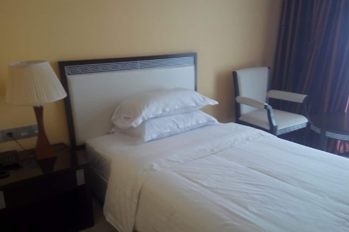 A neatly made bed with white linens, a bedside lamp, and a chair to the right.