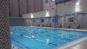 Una piscina con carriles delimitados, un muro con azulejos y una zona junto a la piscina con sillas y un flotador.