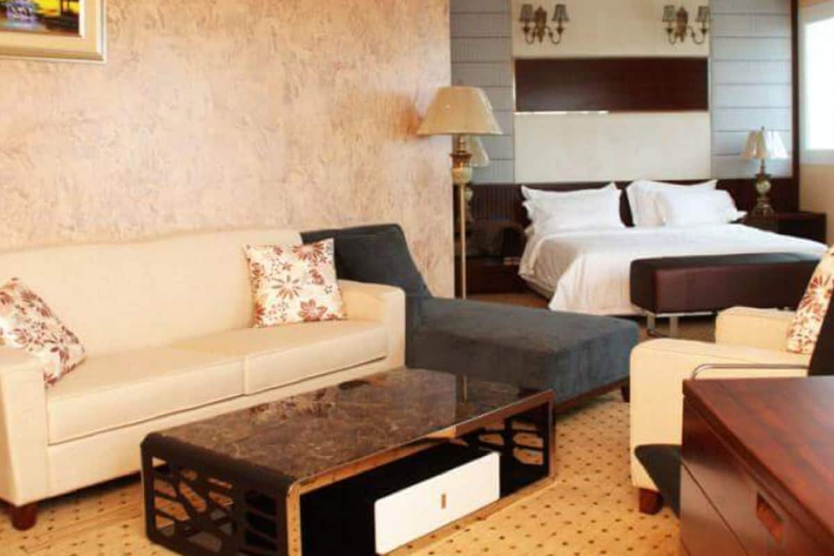 A hotel room with a sofa, a bed, a nightstand, and a lamp.