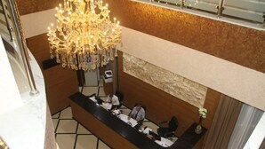 Zona de recepción de un hotel con una araña de cristal, un mostrador de recepción y un área de estar.