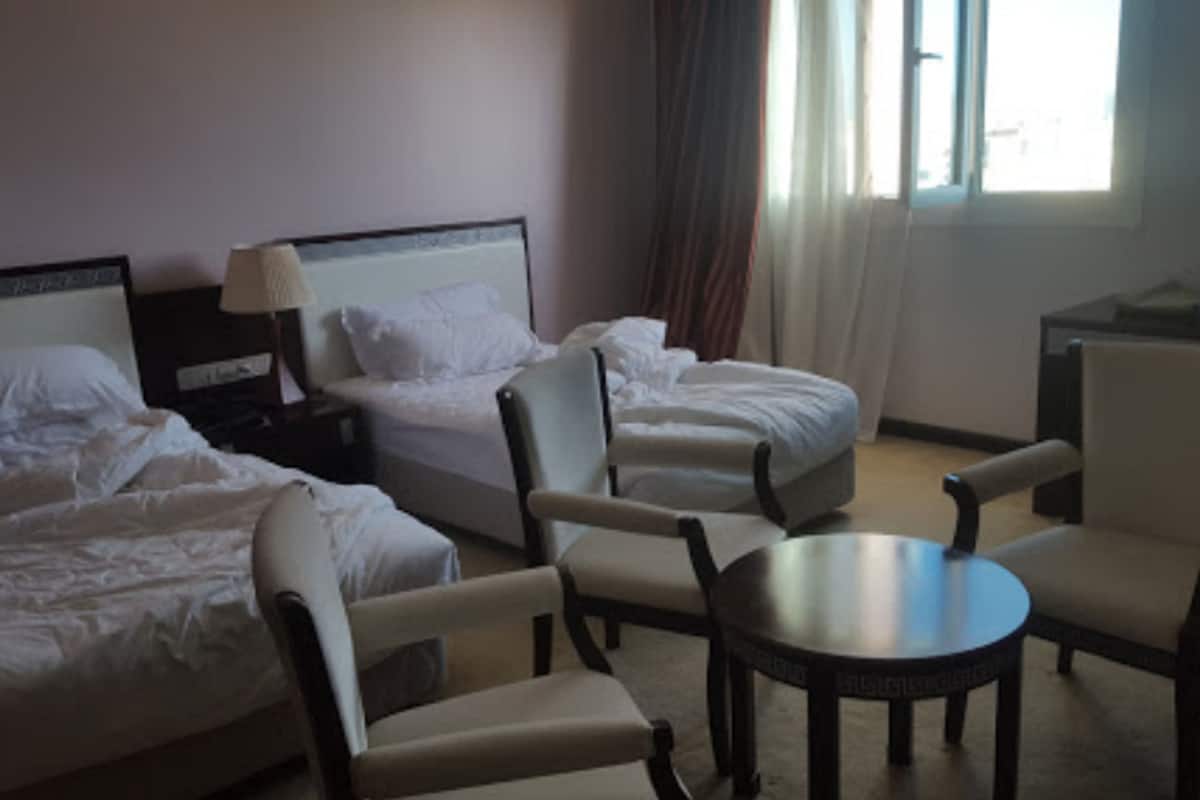 A hotel room with two beds, a desk, a chair, and a small table.