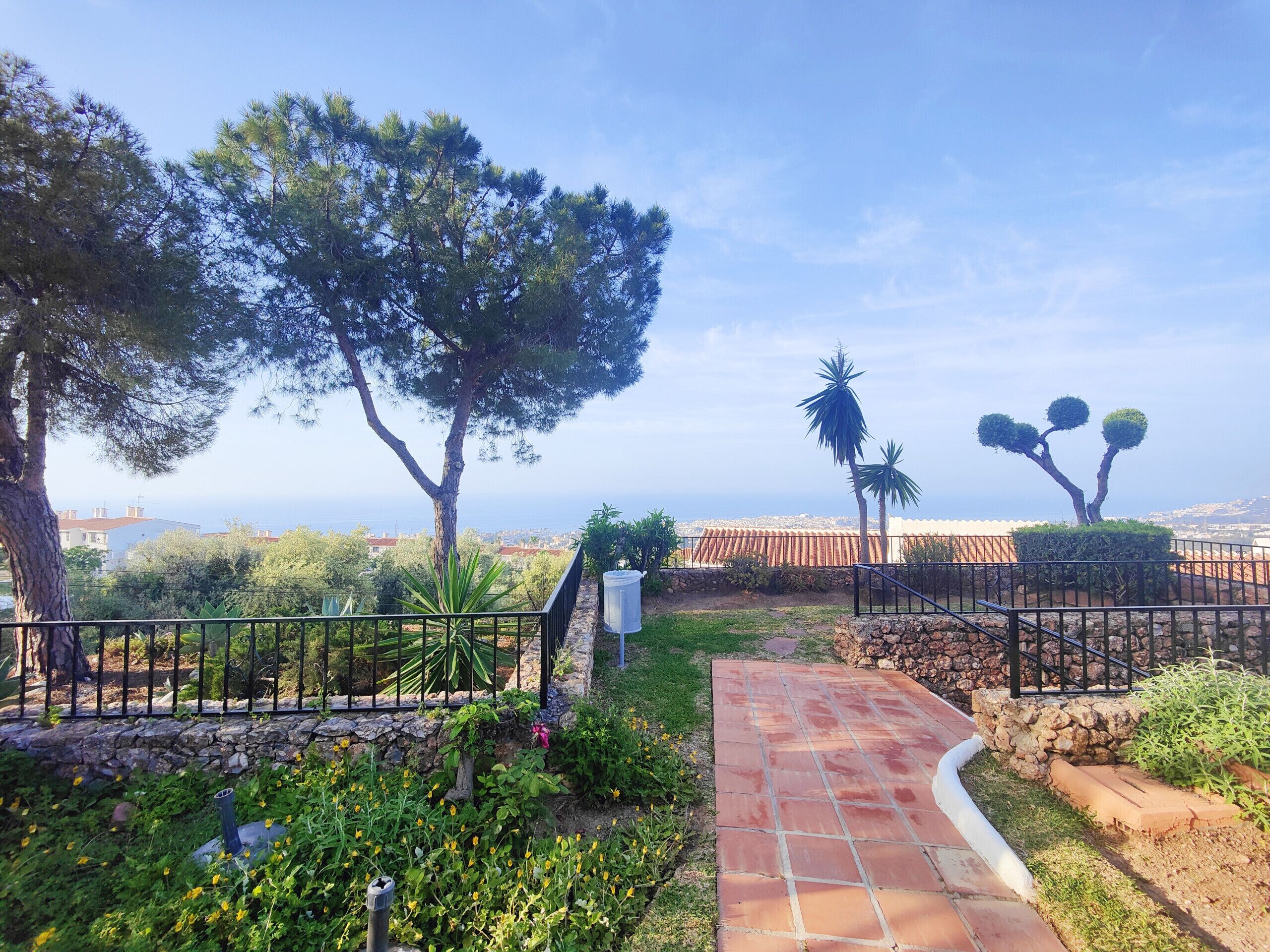 A garden pathway leading to a scenic overlook with a view of the sea and distant buildings.