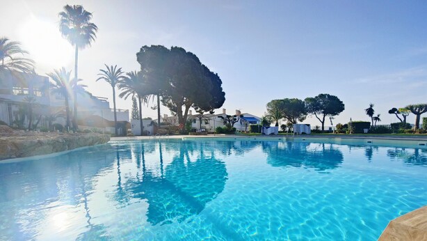 A clear swimming pool with a wooden deck edge, surrounded by palm trees and a clear sky. - AP197 - Capuchinos - Beautiful apartment with Jacuzzi and free Wi-Fi (Nerja)