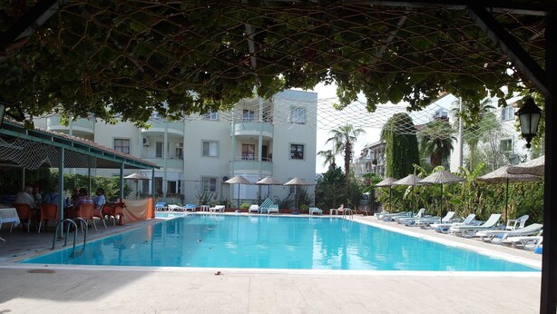 A swimming pool with lounge chairs and umbrellas, surrounded by a covered seating area and a building with balconies. - Akdeniz Apart Hotel (Alanya)