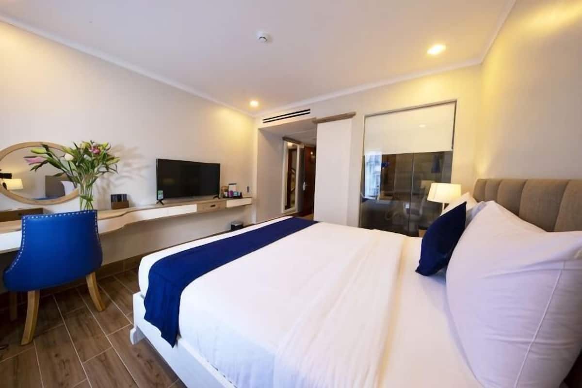 Une chambre d’hôtel avec un grand lit, un bureau avec une télévision, une chaise et un miroir.