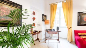 A room with a desk, a chair, a red sofa, a large plant, and a window with yellow curtains.
