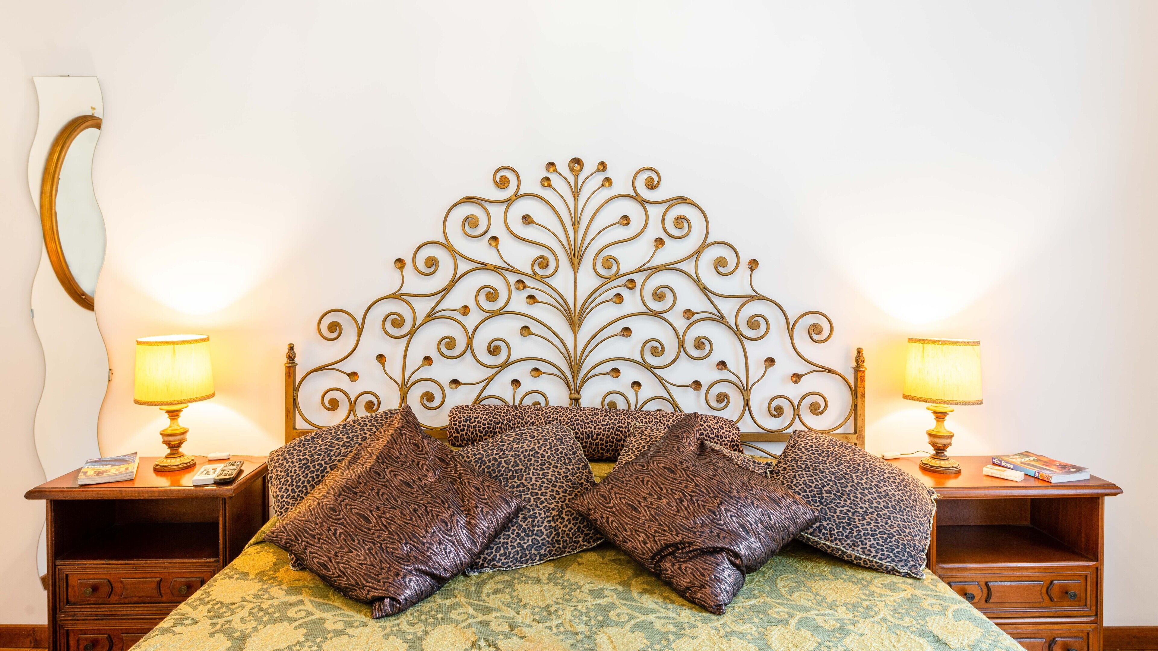 A bed with a decorative headboard, two bedside tables with lamps, and a mirror on the wall.