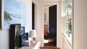 Un couloir doté d’un plancher en bois, d’une lampe blanche, de tableaux encadrés et d’une porte noire donnant sur une autre pièce.