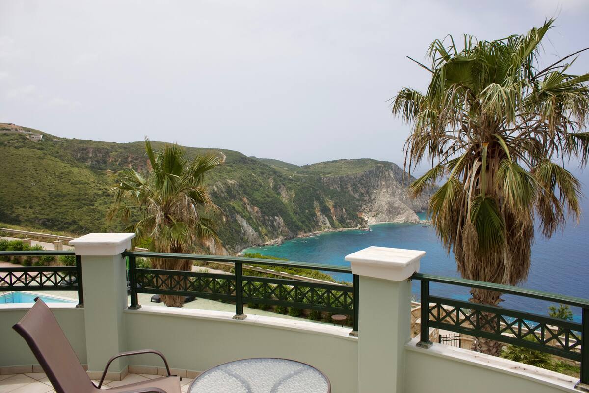 A balcony with a view of a coastal landscape, including a pool and palm trees.