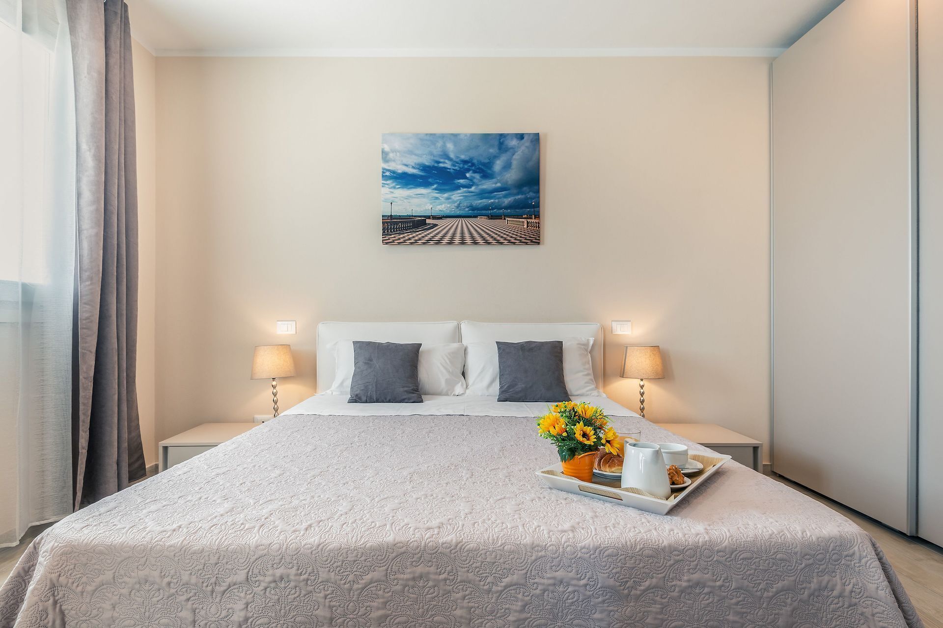 Une chambre d’hôtel avec un lit, deux lampes de chevet, un tableau au mur et un plateau contenant des articles pour le petit-déjeuner.