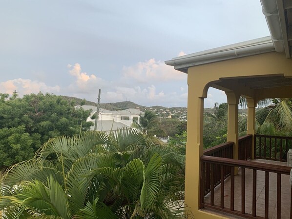 A balcony with a view of a house and surrounding greenery.