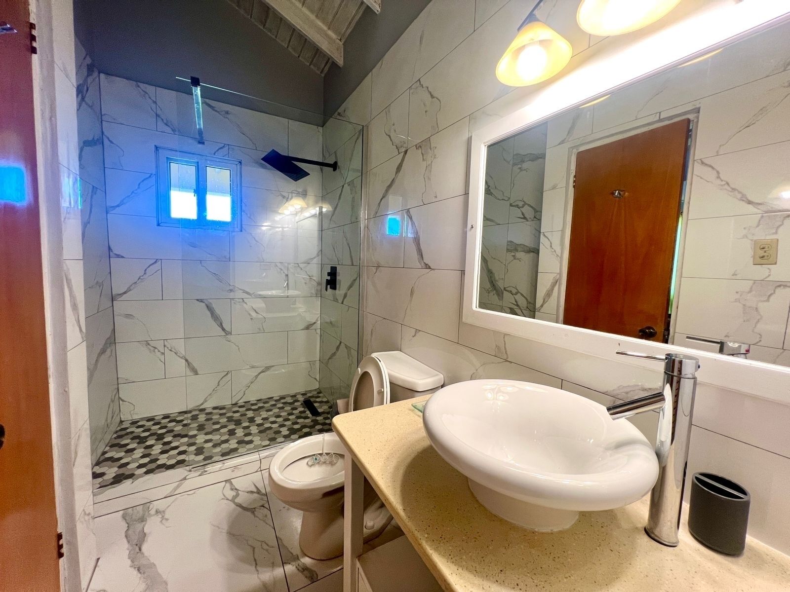 A bathroom with a marble wall, a sink, a toilet, and a shower.