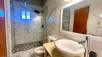 A bathroom with a marble wall, a sink, a toilet, and a shower.