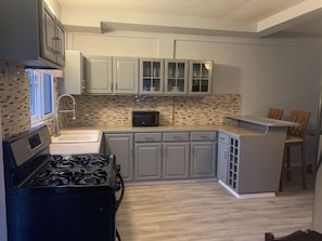 A compact kitchen with white cabinets, a microwave, a stove, and a small dining area with two chairs.