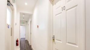 A hallway with white doors, a fire extinguisher, and a fire alarm on the wall. - The Broadway Hotel - London Heathrow (Southall)