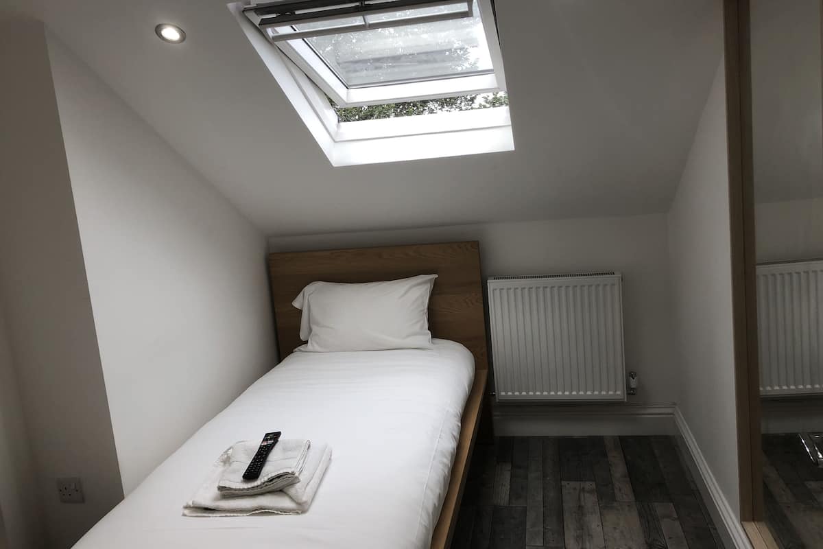 A small, modern bedroom with a skylight, a wooden headboard, a white bed, and a white radiator.