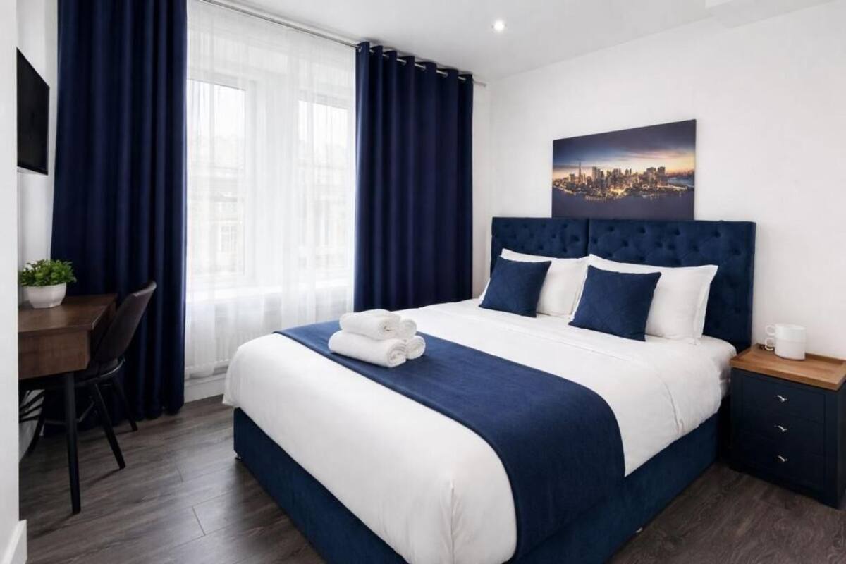 A hotel room with a large bed, a desk with a chair, a small table, and a nightstand.