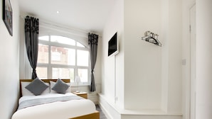 A modern bedroom with a wooden bed, a nightstand, a TV mounted on the wall, and a window with curtains. - The Broadway Hotel - London Heathrow (Southall)