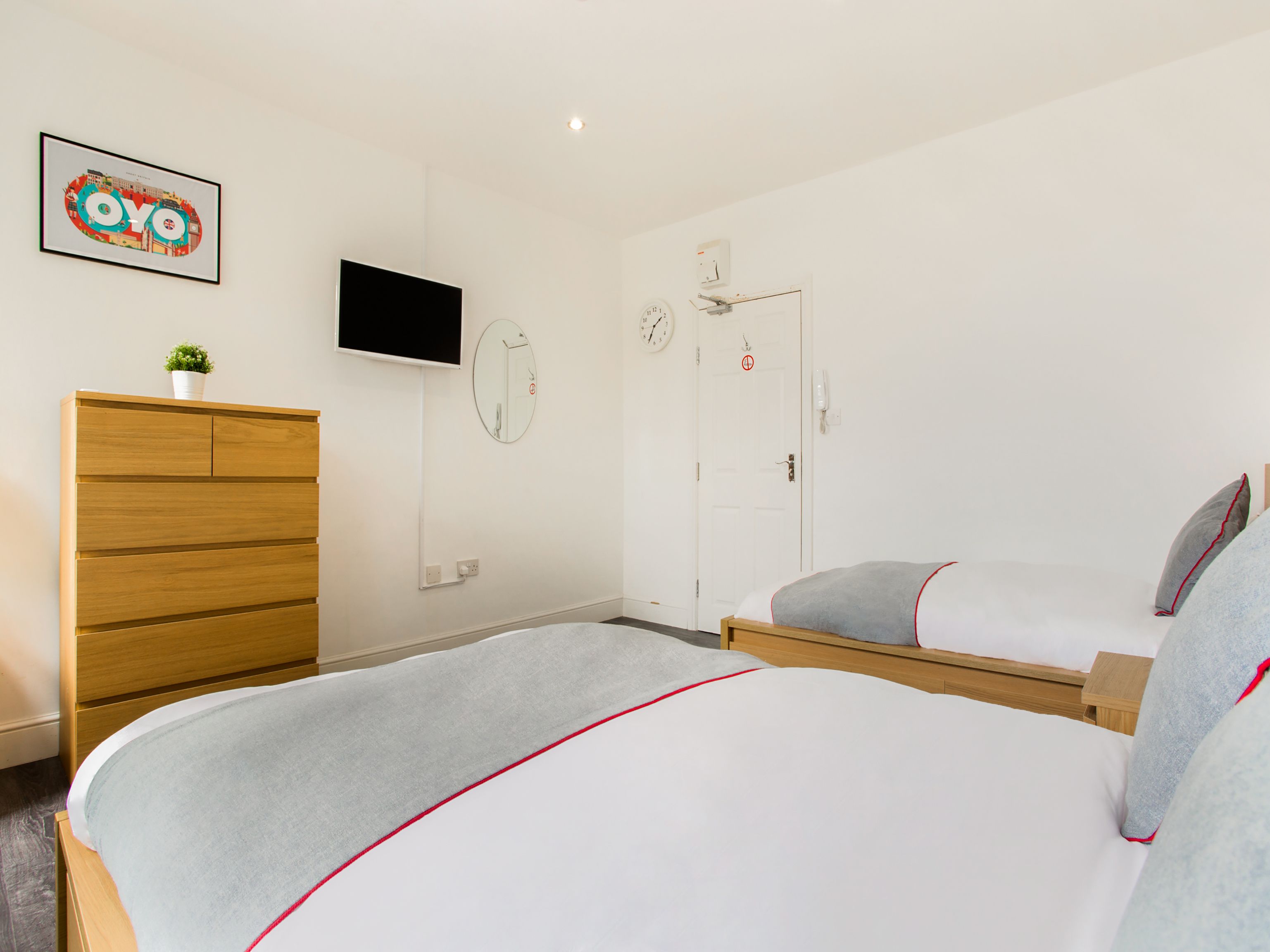 A bedroom with a bed, a wooden dresser, a TV, a mirror, and a door.