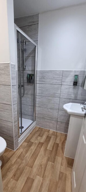 Un baño moderno con cabina de ducha de vidrio, un lavabo blanco y suelo de madera.