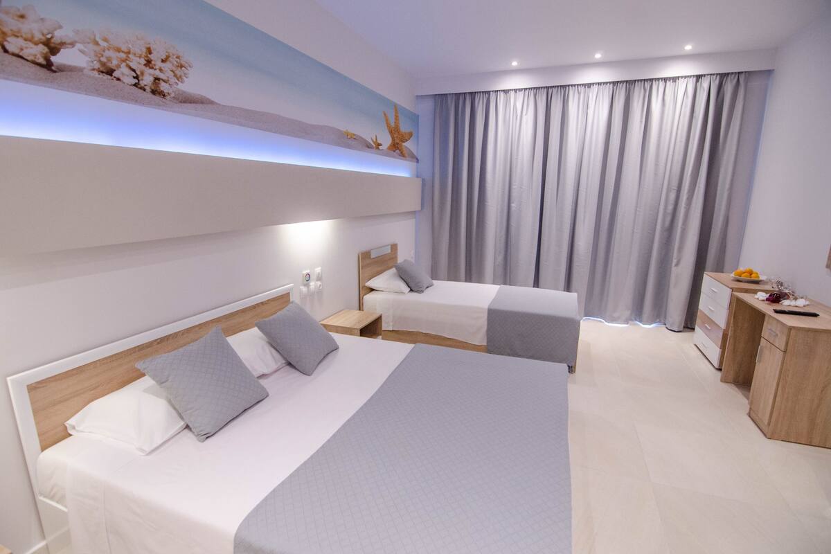 A modern hotel room with two beds, a desk, and a large window with curtains.