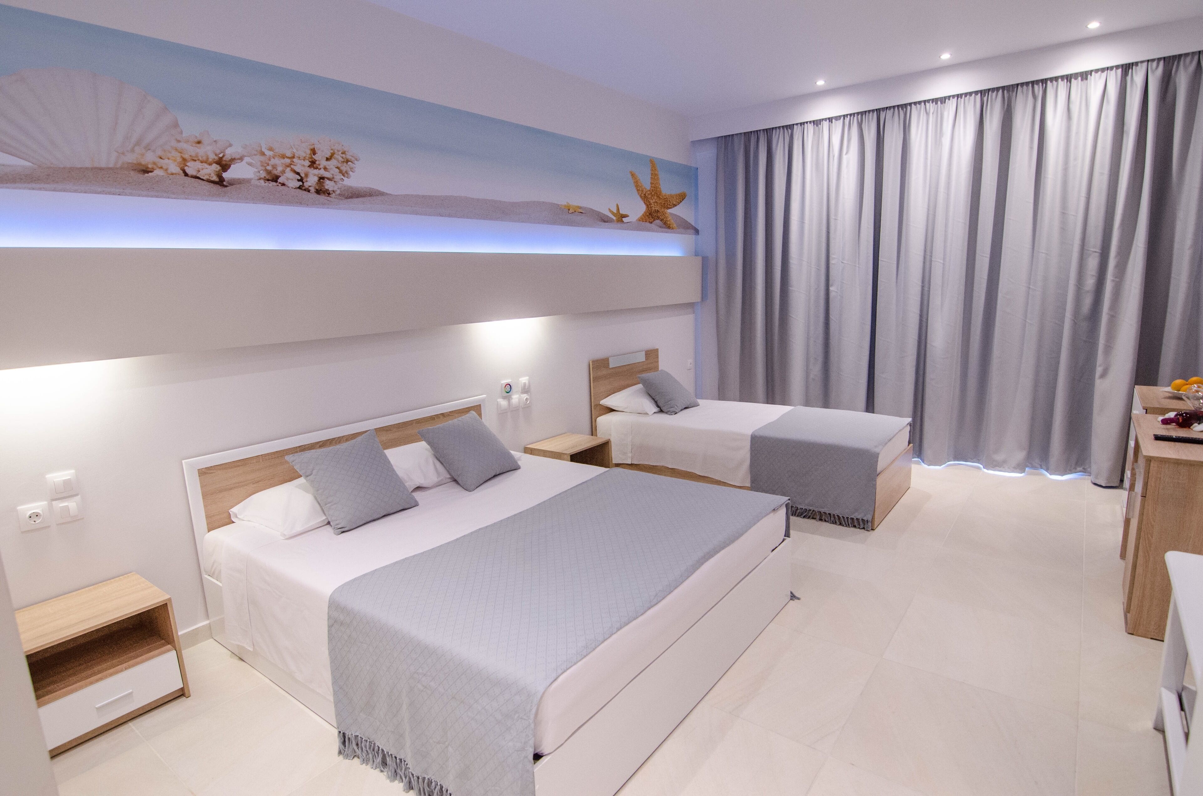 A modern hotel room with two beds, a small desk, and a nightstand.