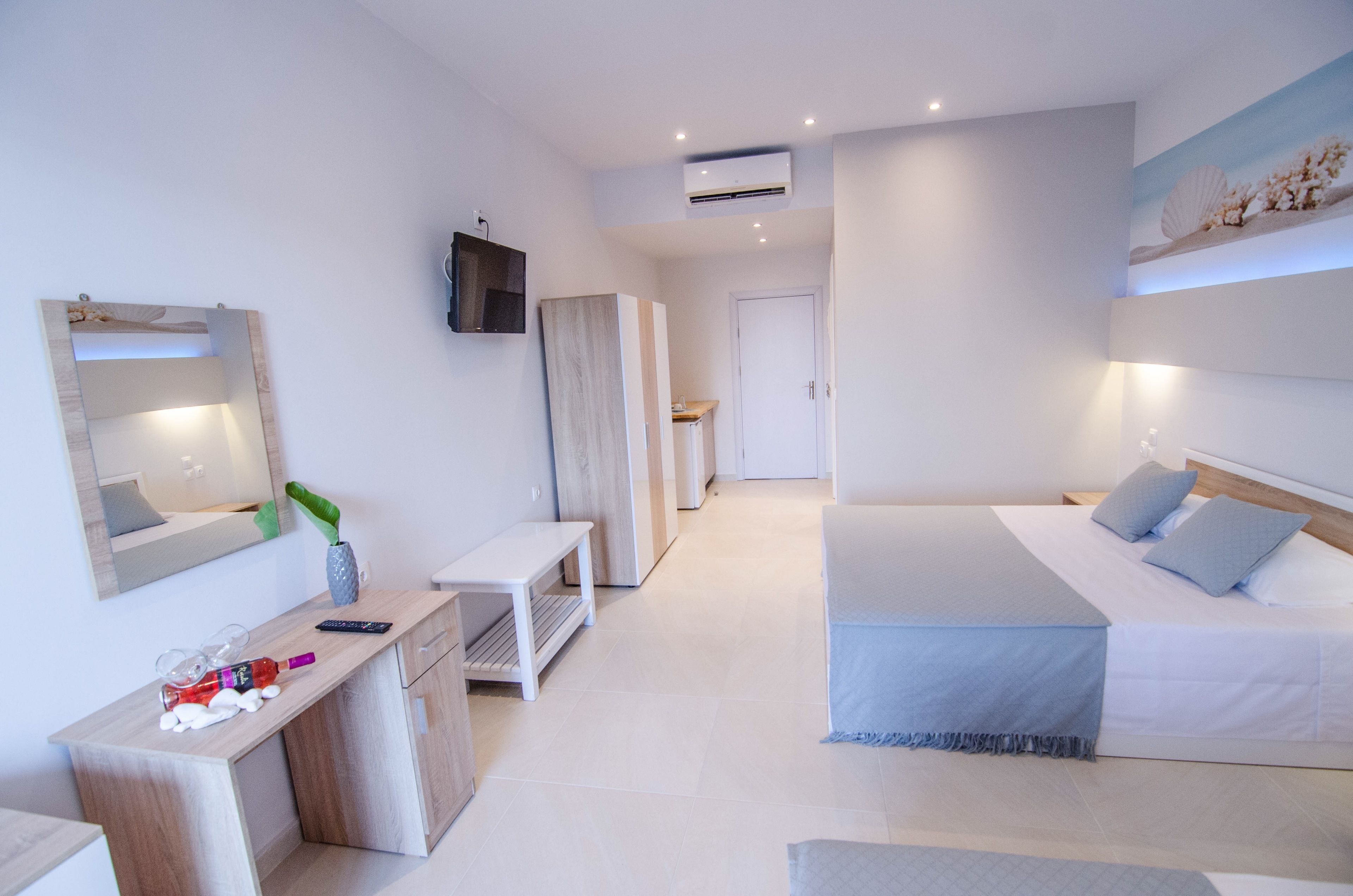 A modern bedroom with a large bed, bedside tables, a TV mounted on the wall, and an air conditioning unit.