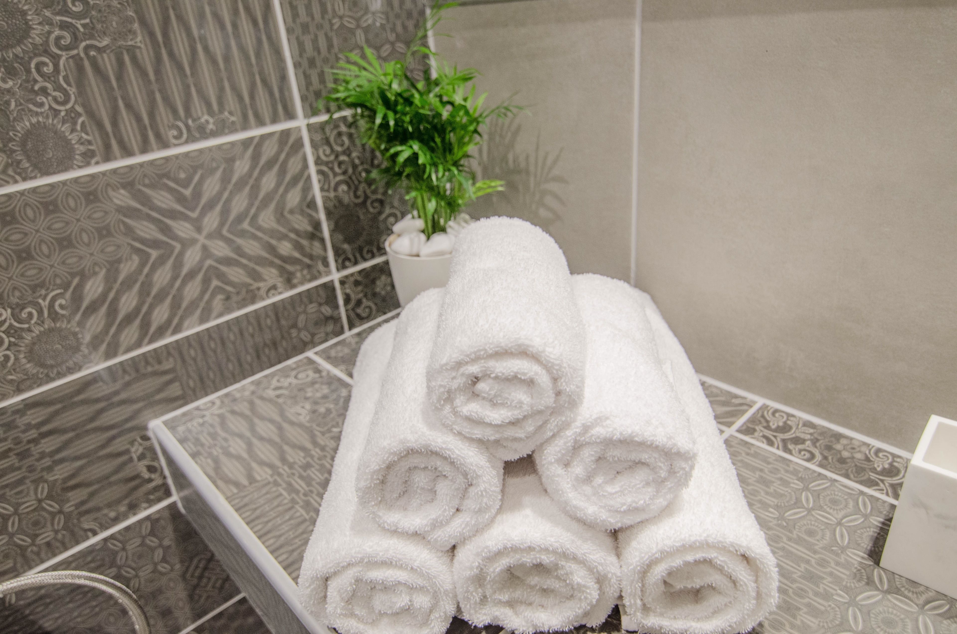A stack of white towels in a bathroom with patterned tiles and a potted plant.