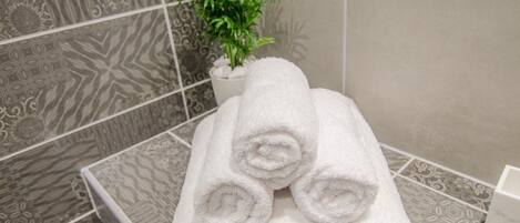 A stack of white towels in a bathroom with patterned tiles and a potted plant.