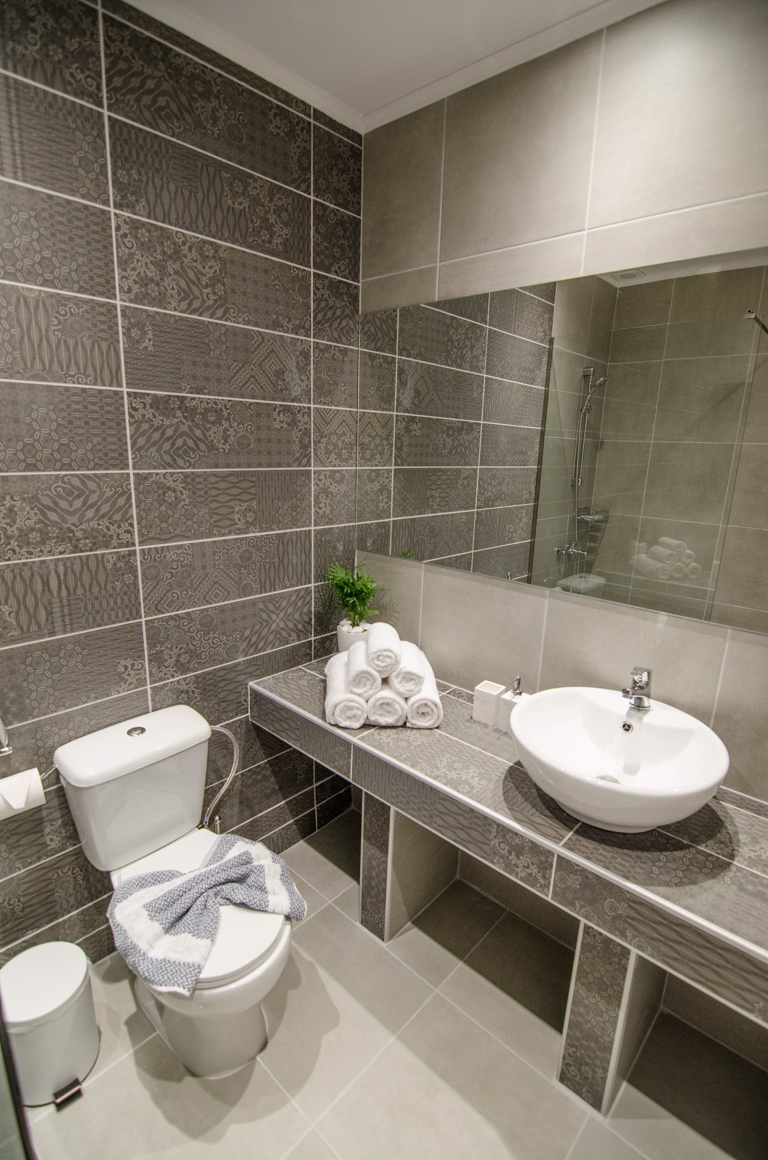 Um banheiro moderno com azulejos estampados, vaso sanitário, pia e espelho.