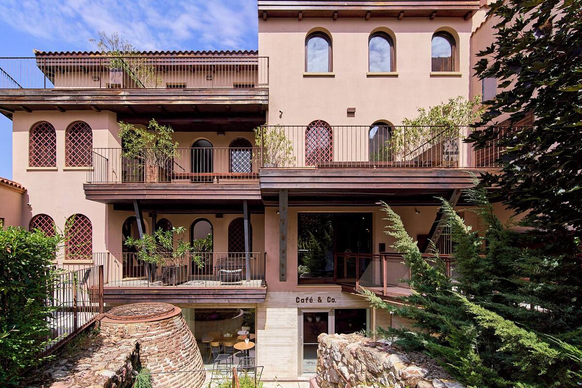 A multi-story building with balconies, arched windows, and a café at the ground level.