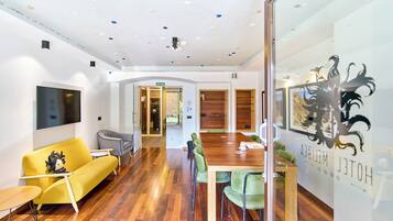 Un interior moderno con piso de madera, un sofá amarillo, una mesa de madera y una pared de vidrio con un logotipo.