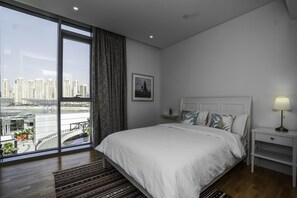 A modern bedroom with a large window, a bed, a nightstand, and a view of a cityscape. - Bluewaters Island (Dubai)