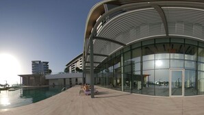 Un edificio moderno con fachada de vidrio curva y un área de piscina al frente.