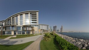 Un edificio moderno con arquitectura curvilínea, un sendero pavimentado y vista al mar.