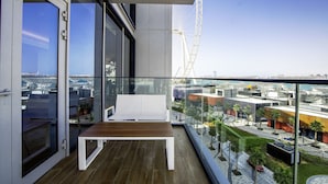 Un balcón con mesa de madera y sofá blanco, con vistas a un paisaje urbano y una noria.