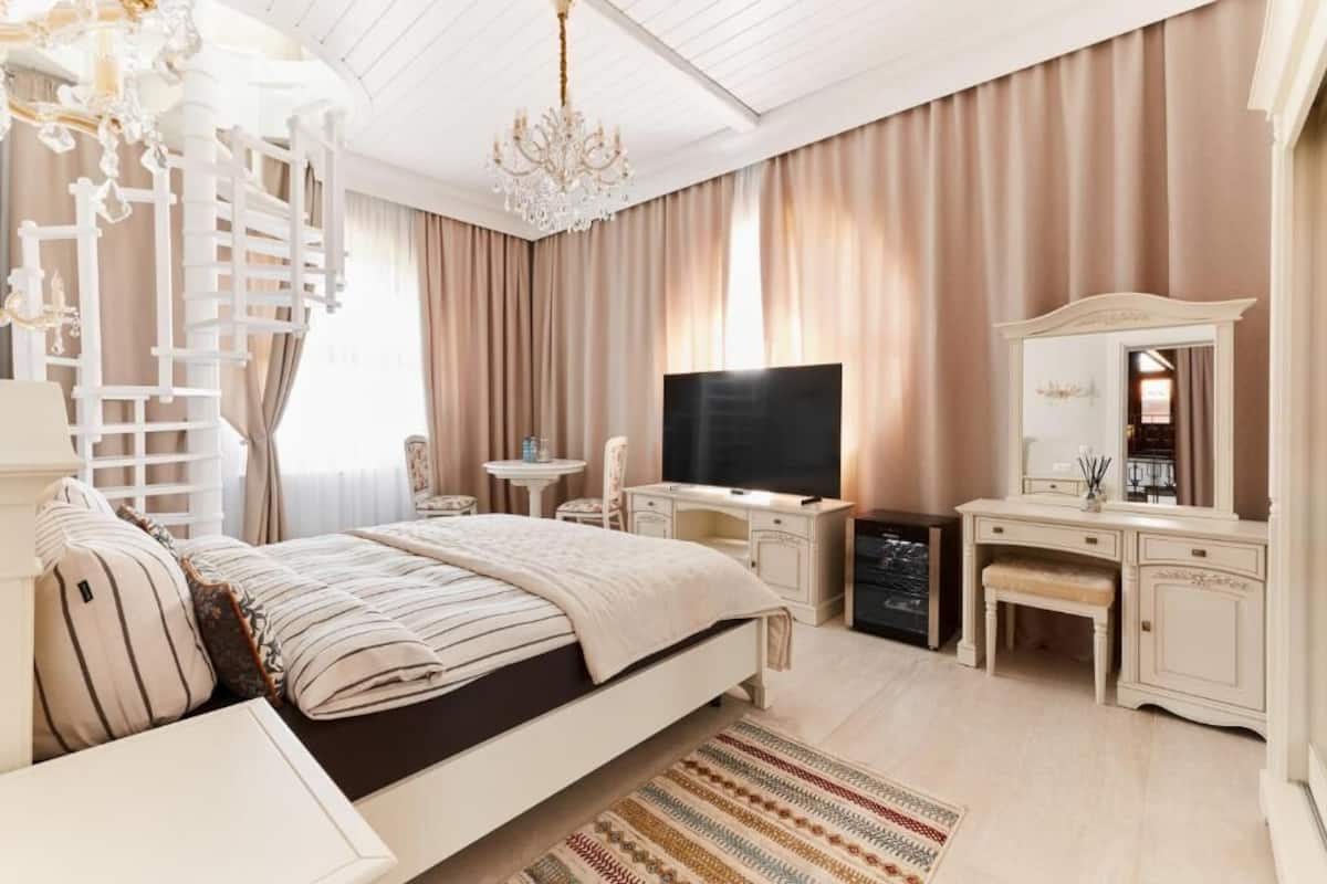 A spacious bedroom with a large bed, a TV, a desk, and a vanity.