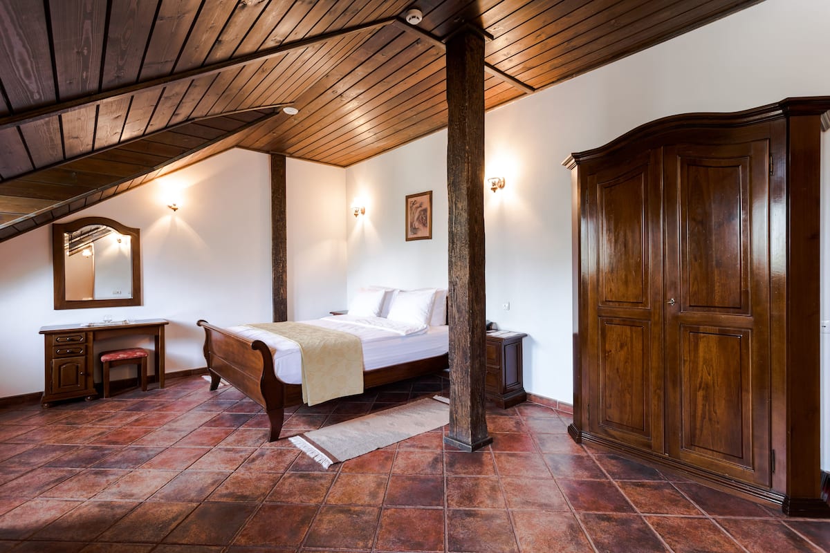 A bedroom with a wooden ceiling, a bed, a desk, and a wardrobe.
