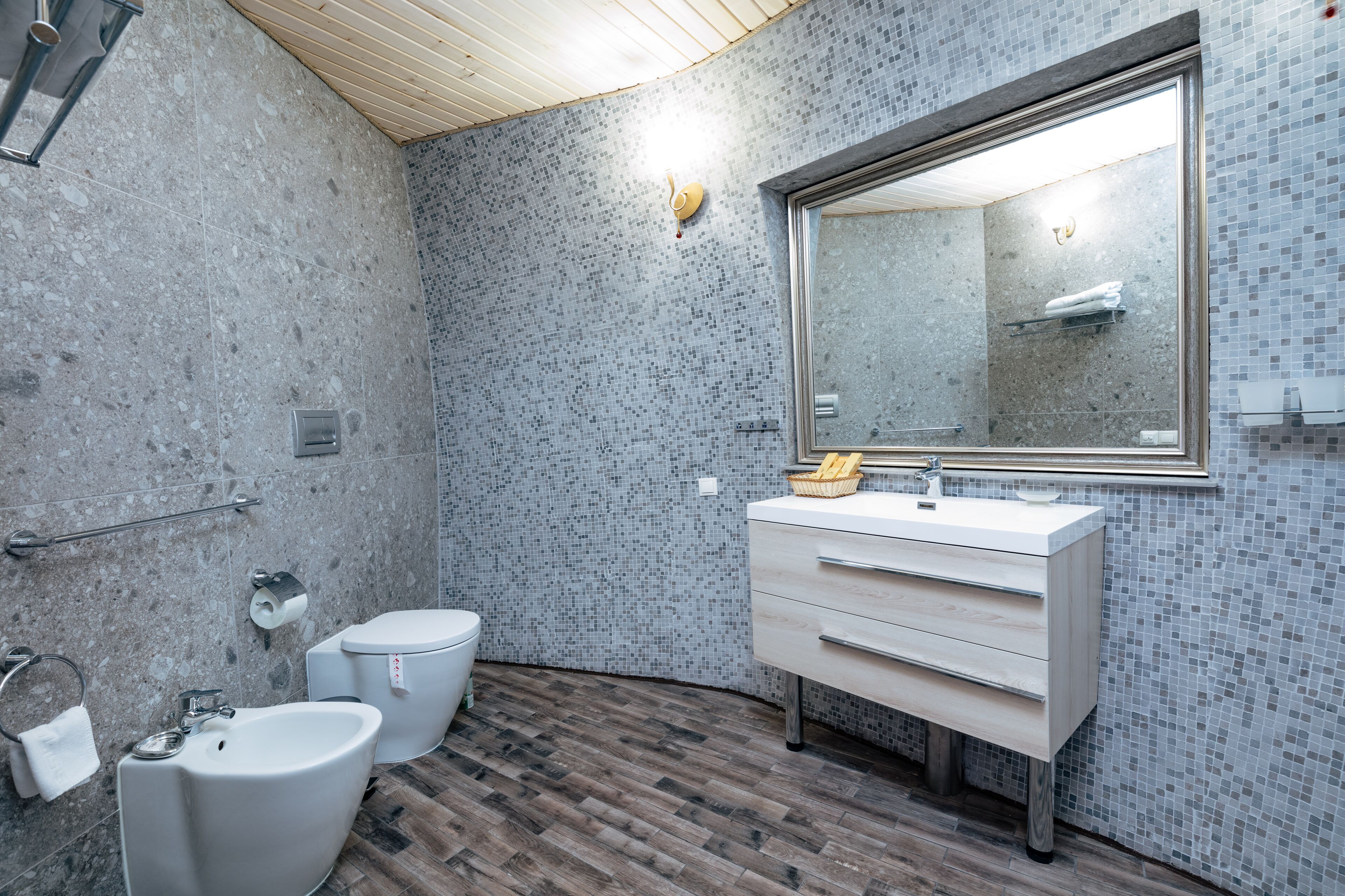 Un baño moderno con techo de madera, un espejo grande, un lavamanos y un bidé.