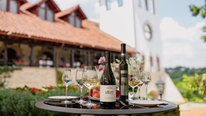 Una mesa servida con copas de vino y botellas, un plato de fruta, y un área de comedor con vistas a un edificio con una torre de reloj.
